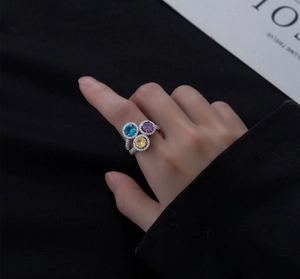 Close-up of three-color gemstone ring set in silver on hand against dark background