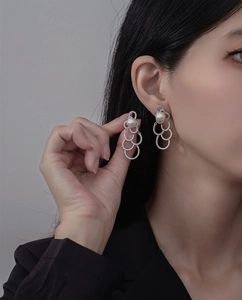 Détail de boucles d'oreilles argentées avec anneaux en cristal et perle blanche