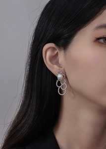 Gros plan sur boucles d'oreilles perles avec trois anneaux entrelacés sertis de pavés