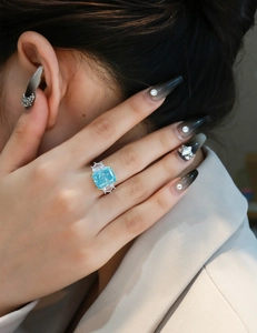 Detail of 13ct light blue cushion cut diamond ring with gold prongs on model's hand