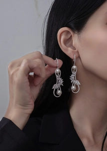 Détail de boucles d'oreilles signe infini en argent avec perles et zircons feuilles