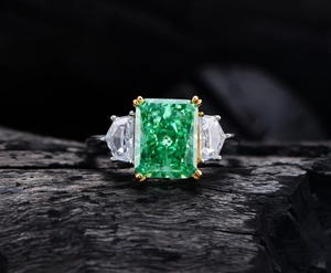 Makroaufnahme: Smaragdgrüner Ring mit Radiant-Schliff auf schwarzem Holzkohle-Hintergrund