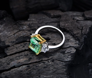 Nahaufnahme Ring mit grünem Stein im Smaragdschliff und Seitenteinen auf Holz