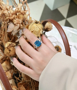 Detailed shot of emerald-cut blue stone ring with triangular side stones on finger