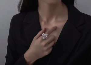 Détail d'une bague fleur en argent S925 sertie de cristaux, portée avec un costume noir