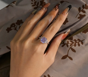 Detailaufnahme eines Rings mit violettem rechteckigem Edelstein am Finger