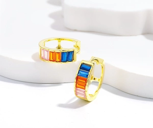 Macro detail of gold hoop earrings with baguette-cut pink, orange, and blue gemstones