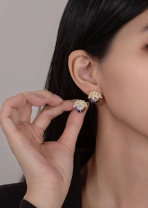 Detail view of sunflower rainbow zircon stud earrings worn and held by a model
