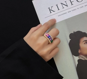 Detail view of gold ring with colorful rectangular gemstones worn by a model