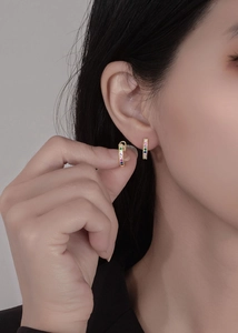 Detailed view of gold huggie earrings with rainbow colored stones on ear