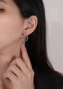 Close-up of teardrop stud earrings featuring colorful rainbow zircons on a female model