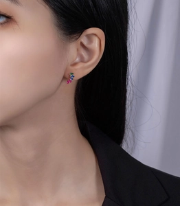 Detail of leaf-shaped earring with red, blue and green crystals on model's ear