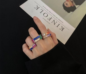 Close-up of stacked gold rings with multi-colored rectangular baguette zircons on fingers