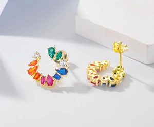 Detail van C-vormige gouden oorbellen met kleurrijke zirkonia stenen in diverse vormen