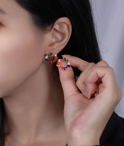 Detailopname van regenboog C-vormige oorbellen met kleurrijke edelstenen op een model