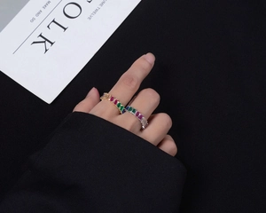 Close-up of two stacked gold eternity rings with colorful baguette-cut rainbow gemstones