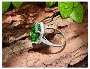 Macro d'une bague avec grosse pierre verte taille émeraude et diamants sur écorce d'arbre