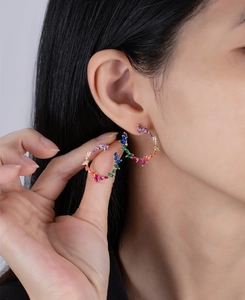 Close-up of golden olive branch hoop earrings with vibrant multi-colored marquise zircons