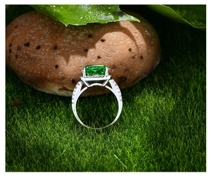 Gros plan d'une bague avec émeraude et pavé de diamants sur de la mousse naturelle