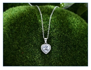 Dettaglio della collana con cuore in argento e zircone su sfondo di muschio verde