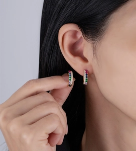 Détail de boucles d'oreilles créoles dorées avec pierres arc-en-ciel portées à l'oreille