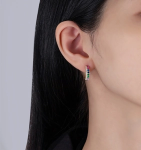 Détail de boucle d'oreille huggie dorée avec pierres arc-en-ciel et zircon sur l'oreille