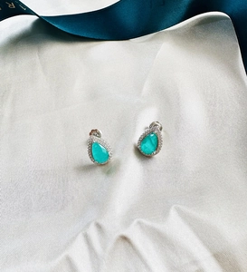 Detailed close-up of 925 silver pear cut green emerald stud earrings on white silk fabric