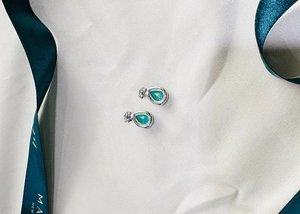 Detail of pear-cut emerald earrings with silver setting on soft silk fabric and ribbon