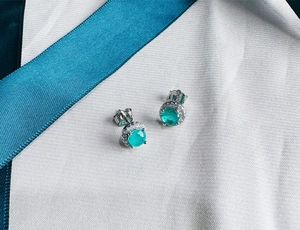 Detailed view of 5mm green emerald stud earrings with a halo of diamonds on fabric