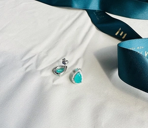 Macro view of teardrop emerald halo earrings in 925 sterling silver on white satin fabric