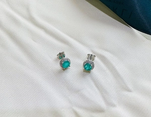 Macro shot of silver stud earrings featuring 5mm green emerald with diamond halo