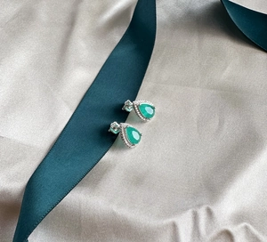 Macro detail of pear-cut emerald earrings with silver setting on elegant satin background