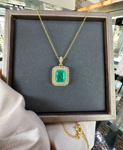 Detail of emerald-cut green gemstone pendant with double halo on 18k gold chain