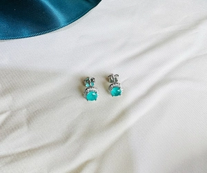 Detailed close-up of 925 silver stud earrings with round green gemstones and halo diamonds