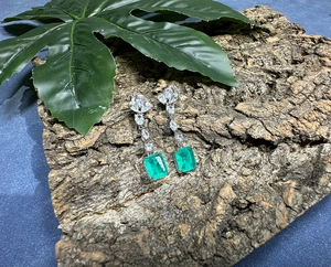 Detailed macro view of emerald-cut green gemstone earrings on rustic wood bark