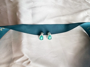 Macro detail of pear-shaped emerald stud earrings with diamond halo on green ribbon