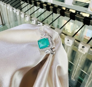 Detailed macro view of an emerald-cut green gemstone ring on champagne silk fabric