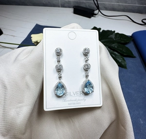 Macro shot of 925 silver teardrop earrings with blue topaz and pavé stones on display card