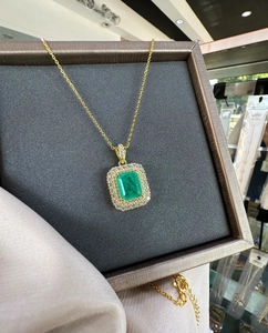 Close-up of emerald cut green gemstone pendant with double halo diamonds in gold necklace