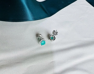 Close-up of 925 silver stud earrings with 5mm emerald-cut green stone and halo crystals