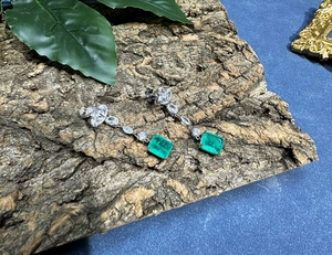 Detail of emerald drop earrings on rustic bark base with elegant cluster setting