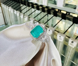 Macro detail of emerald-cut green gemstone ring with side diamonds on champagne satin