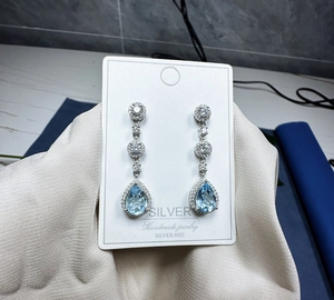 Macro view of pear-cut blue topaz earrings in S925 sterling silver with halo diamonds