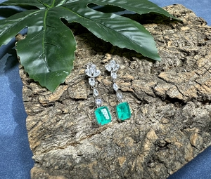 Macro detail of silver drop earrings featuring emerald-cut green stone and CZ leaf accent