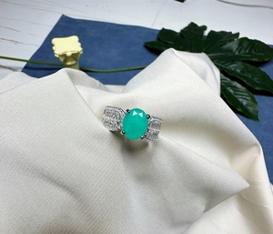 Gros plan détaillé d'une bague avec pierre verte ovale et pavage sur tissu blanc