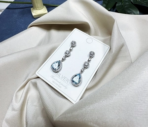 Close-up of S925 silver pear-shaped light blue topaz drop earrings on satin fabric