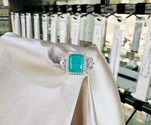 Macro detail of rectangle cut emerald ring with pavé zircons on satin display