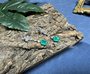 Macro detail of silver drop earrings with emerald gemstones on rustic bark