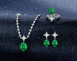 Detailed view of emerald necklace, ring and earrings set on dark blue starry background