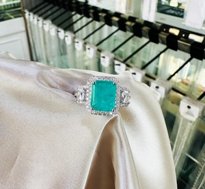Detailed view of emerald cut green gemstone ring on champagne satin background